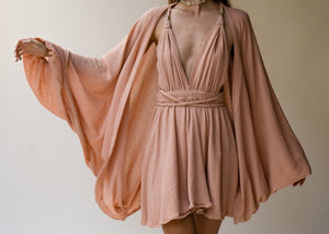 Woman wearing a flowing peach dress with a matching jacket against a plain background in Tulum style wearing ELLECHEMY