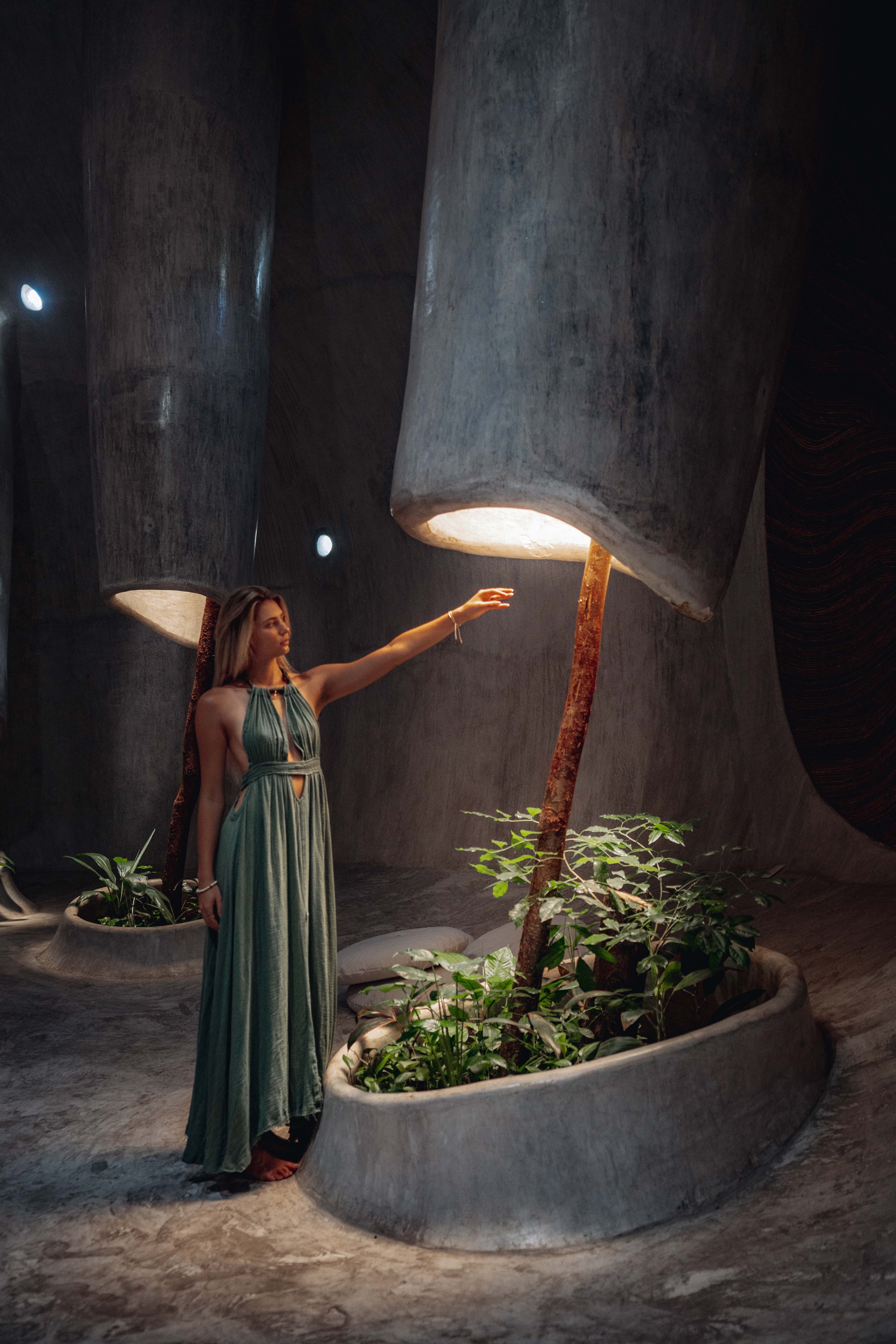 Woman in a green dress standing next to a large concrete lamp at Azulik Tulum.