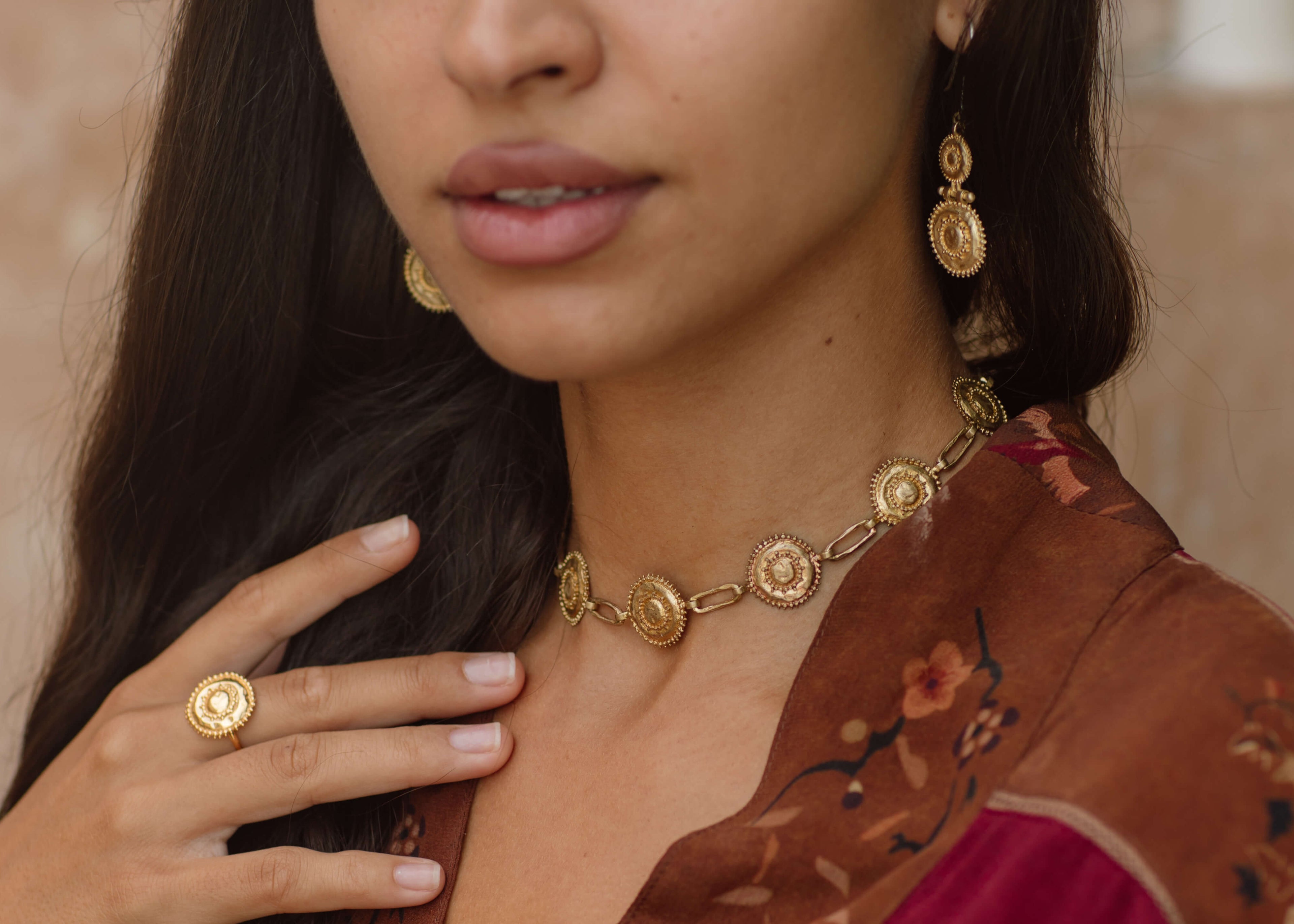 Woman wearing gold jewelry including earrings, necklace, and ring against a neutral background from the Nakila Collective curated by Ellechemy in Tulum at our flagship store on Calle 07 in la Veleta