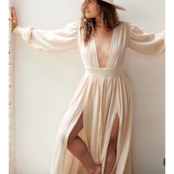 Woman wearing a flowing beige Ellechemy dress with a white hat against a light background. Ellechemy Lagertha Dress Ethereal White White Cotton Maxi Dress | Casual Beach Boho Dress 